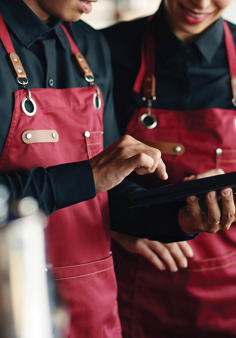 Two people wearing red aprons are looking at a tablet computer. AI generated content