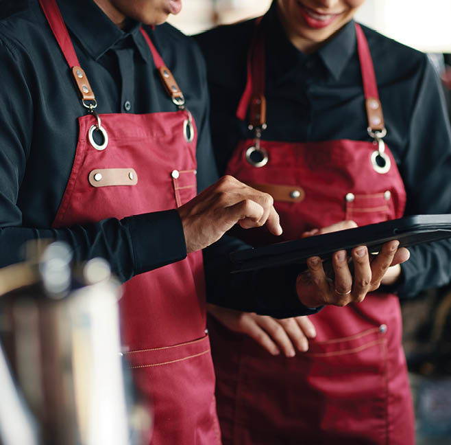 Two people wearing red aprons are looking at a tablet computer. AI generated content
